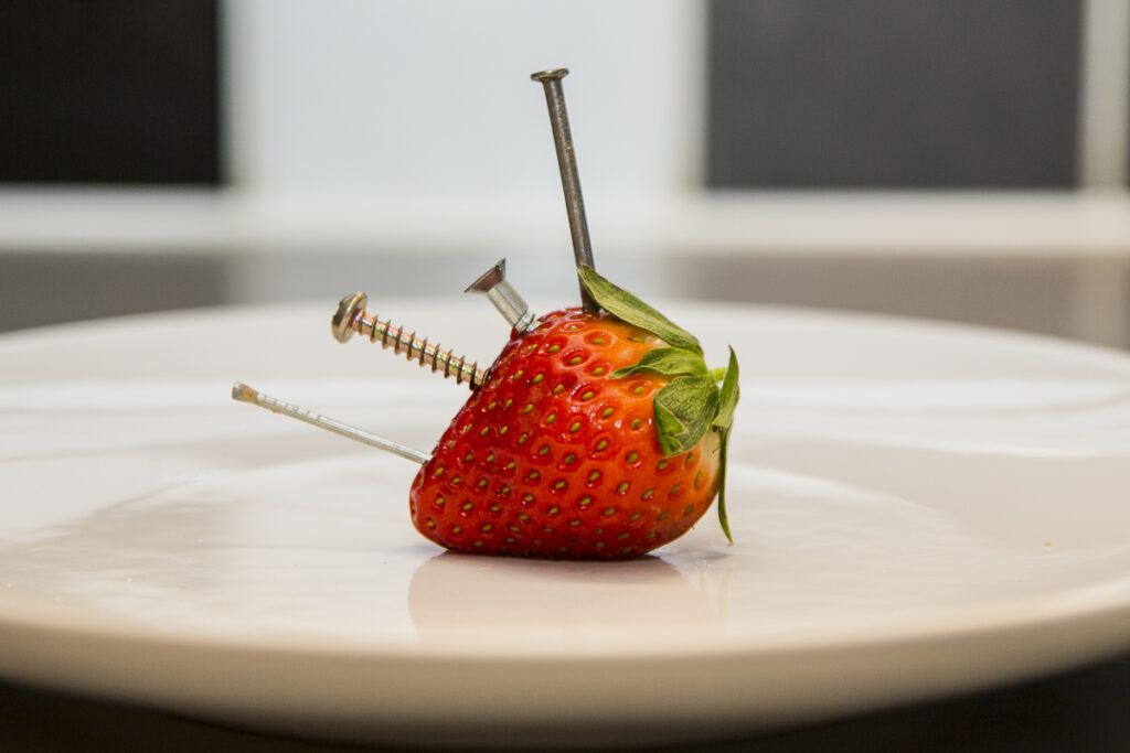 A strawberry with various pieces of tramp metal sticking out of it.